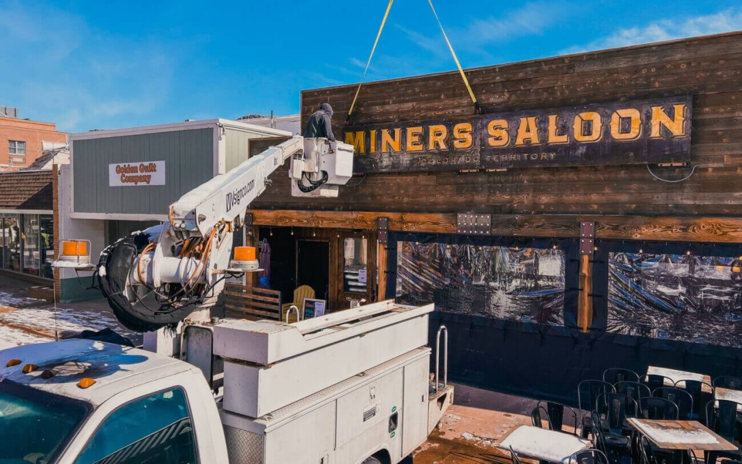 Sign installation crew lifting a large custom wall sign for Miners Saloon in Golden, CO — outdoor sign installation by Vision Visual Signs